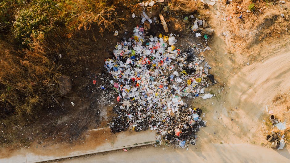 A large collection of overflowing waste bins and a significant pile of mixed rubbish, including cardboard boxes, plastic bags, paper, and miscellaneous packaging materials, situated in a designated ou